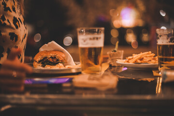 Dettaglio primo piano panino hamburger, patatine fritte e bicchiere di birra fresca su tavolo in...