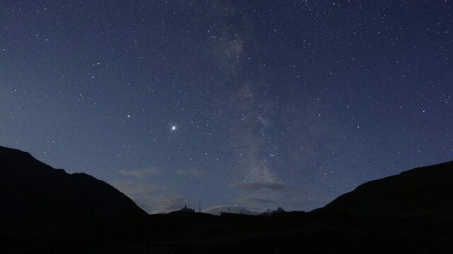 Starry sky and milky way in the mountains. Mountain village against the background of the night starry sky and the milky way. Time Lapse video.
