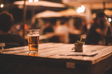 Dettaglio bicchiere di birra fresca poggiata su tavolo in legno di un locale notturno all'aperto 