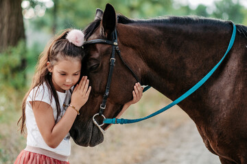 Obraz premium Friendship of a child with a horse. A little girl is affectionately stroking her horse. Walking girls with a horse in the park in autumn.