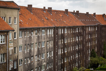 Rows of old generic five story residential buildings with v shaped roofs in the city of Berlin. Apartments built in the 50s and 60s with worn facades seen in a row from far away, in horizontal format