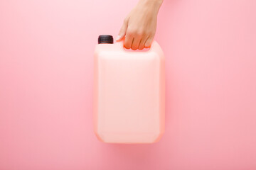 Young woman hand holding 5 L plastic container on pink table background. Pastel color. Cleaning...
