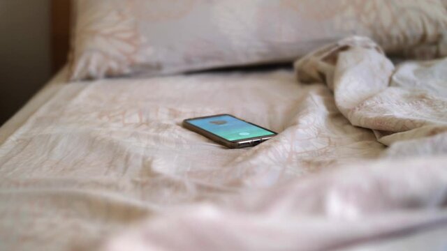 Smartphone that Starts Ringing above an Unmade Bed and a Hand Grabbing it