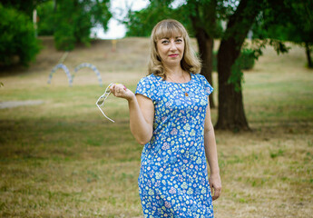 A young blonde woman in a blue dress holds glasses in a white frame