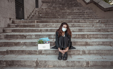 Sad woman in face mask with office box feeling hopeless after losing job due to coronavirus job cuts