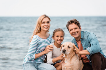 Family with golden retriever looking at camera on beach
