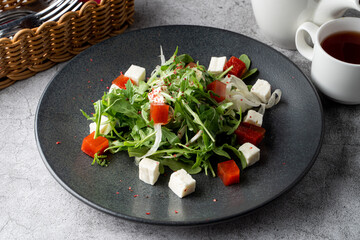 Classic dietary salad with arugula, tomatoes and fresh feta on a wide black restaurant plate