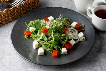 Classic dietary salad with arugula, tomatoes and fresh feta on a wide black restaurant plate