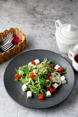Feta and arugula salad on a black plate, top view photo on grey stone background