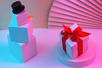 The polygonal snowman of cubes and gift is illuminated with neon light, against the background of the fan. Trend Concept 2020, 2021.