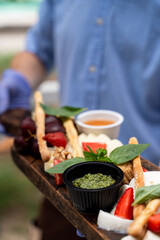 Waiter in a blue shirt and blue rubber gloves is holding a wine platter with gourmet snacks, restaurant service during coronavirus