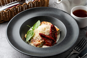 Yummy italian lasagna with bechamel sauce in a black wide plate, top view, close up