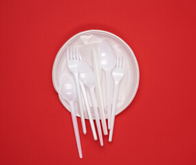 round plate and stack of plastic forks and spoons on red background