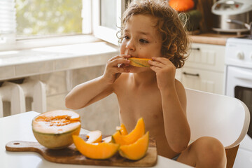 Cute beautiful little boy eating fresh melon. Healthy food, childhood and development. 