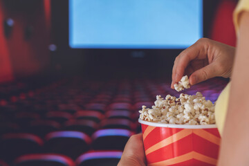 A young woman is watching a movie and is eating popcorn at the cinema