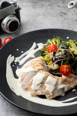 Close up of boiled chicken breast and broccoli, served on a black plate and grey table