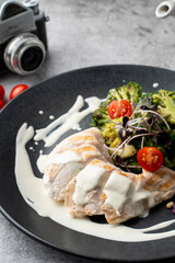 Close up of boiled chicken breast and broccoli, served on a black plate and grey table
