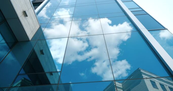 Modern futuristic abstract business building high tower blue glass background with reflected white skies and clouds on wall and clear window of architectural construction mirrored urban design pattern