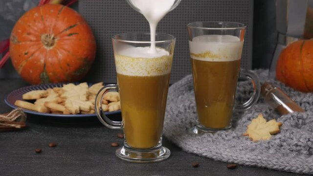 Pouring whipped cream into pumpkin sweet spicy latte with autumn cookies and moka pot coffee maker. Grey knitted plaid