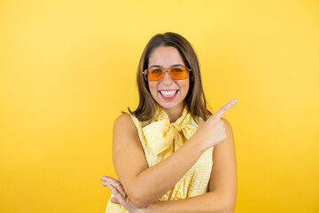 Young beautiful woman wearing sunglasses over isolated yellow background smiling happy pointing with hand and finger to the side