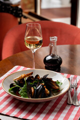 Italian gourmet snack: mussels with spinach and balsamic vinegar with a glass of white wine, wooden table and italian red and white table cloth