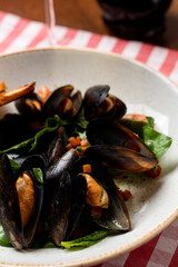 Mussels with spinach and balsamic vinegar with a glass of white wine, wooden table and italian red and white table cloth
