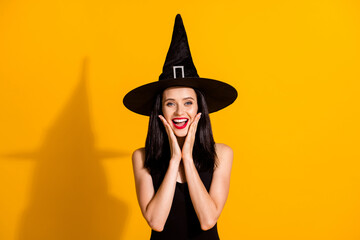 Photo of cute charming young magician lady hands face open mouth excited receive compliment cute costume wear black wizard headwear dress isolated bright yellow color background