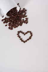Coffee beans spill out of the cup on white background. Coffee heart