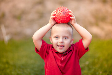 Portrait of a little cute boy with Down Syndrome, a child holding a red ball in his hands, playing...