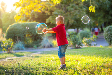 Little cute boy with Down Syndrome plays with huge soap bubbles in the park, a disabled child wants...