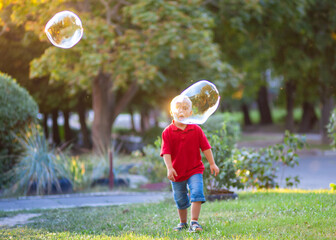 Little cute boy with Down Syndrome plays with huge soap bubbles in the park, a disabled child wants...