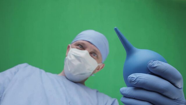 Doctor with an enema. A doctor with an enema in his hands stands above the patient. First-person view, green screen background. Doctors face with an enema in front of a patient