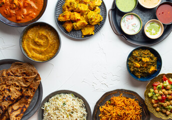 Variety of Indian food, different dishes and snacks on white rustic background. Pilaf, butter chicken curry, rice, palak paneer, chicken tikka, dal soup, naan bread, assortment of chutney. Top view.