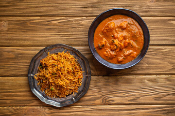 Indian chicken curry in old metal bowl and pilaf with biryani rice on wooden rustic background. Traditional Indian dish butter chicken tikka masala and pilaf, healthy lunch or dinner. Top view.