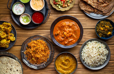 Assorted Indian home food, different dishes and snacks on wooden rustic table. Homemade Pilaf, butter chicken curry, palak paneer, chicken tikka, dal soup, naan bread, choice of chutney. Top view.