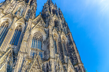 Facade of Cologne Cathedral Roman Catholic Church of Saint Peter gothic architectural style building with spires in historical city centre, blue sky in sunny day, North Rhine-Westphalia, Germany