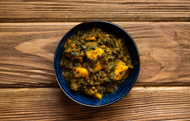 Indian Palak paneer on wooden rustic background. Traditional Indian dish with cheese paneer and spinach gravy. Healthy vegetarian meal. Top view.