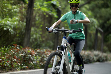 Naklejka premium Woman cyclist looking at her smartwatch while riding bike outdoors on sunny day
