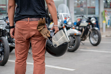 Fototapeta na wymiar Young Biker standing and holding helmet and gloves beside motorcycle.Trip and lifestyle of motorbike concept