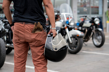 Young Biker standing and holding helmet and gloves beside motorcycle.Trip and lifestyle of motorbike concept