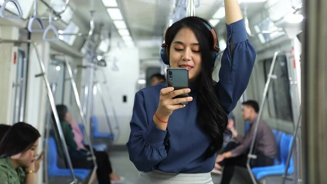 A lifestyle of young Asian woman using cellphone with headset while taking the subway train to work at the rush hour morning