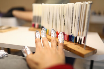 Woman's hand with foil on nails is standing next to samples of varnish with color palette. Gel nail...