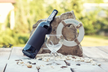 Bottle of wine and wine glass on wooden table with sand and rock.