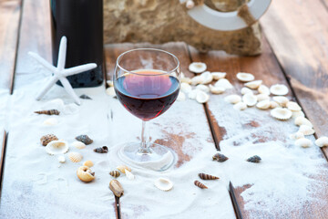 Bottle of wine and wine glass on wooden table with sand and rock.