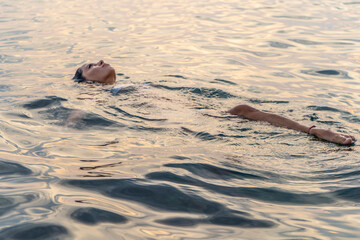 Obraz premium Beautiful young woman portrait floating in the sea at sunset, relaxing
