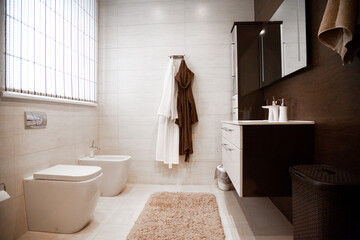 Bright new bathroom interior with glass walk in shower surround, brown vanity cabinet and paired with mosaic tile . Beige and brown tones. comfort