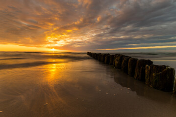 Fototapeta na wymiar beautiful sunset on the Baltic Sea, waves washing the old wooden breakwaters