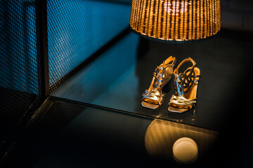 Luxury grey / silver high heel shoes on a glass floor covered in yellow light.