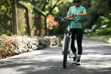 Woman cyclist looking at her smartwatch while riding bike outdoors on sunny day