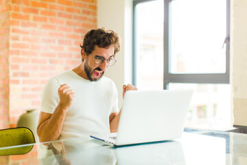 young bearded man with a laptop shouting aggressively with annoyed, frustrated, angry look and...